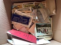 Box filled with vintage postcards, a 1938 embroidered championship patch, assorted papers including a red booklet, and other folded printed materials.