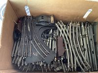 Box of assorted Lionel metal model train tracks and switches showing curved and straight track sections along with large switch bases.