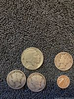 Coins arranged on a dark fabric background showing 3 Mercury dimes, 1 Buffalo nickel, and 1 Indian Head penny and a wheat penny