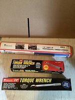 Photo showing three new torque wrenches in original packaging, including a 1/2 inch drive in a cardboard tube, a torque wrench in a black and yellow box, and a 3/8 inch torque wrench in a black box.