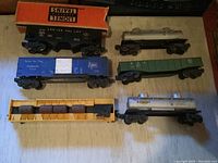 Top view showing six O Gauge train cars including LIONEL branded box, tanker, boxcar, flat cars, and coal hopper.