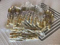 Photo showing a set of new Mikasa utensils including spoons, forks, knives, and teaspoons, all with cream-colored handles featuring floral decoration, packaged in individual plastic wrapping.