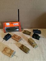 Eight different small plastic military tank models displayed on light surface, including one still in packaging