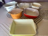 Overview photo of various Pyrex and CorningWare glass bakeware items arranged on a bedspread showing different casserole dishes, bowls, and a citrus juicer.