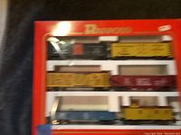 Photo of boxed set of Rivarossi model train cars showing six different cars including boxcars, gondola, passenger car, and caboose in original red packaging with visible Rivarossi branding.
