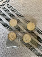 Four silver half dollar coins in protective sleeves on fabric surface, showing fronts.