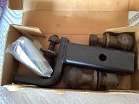 Photo shows metal tow hitch receiver bar, two rusty ball mounts, bolt, and wrapped installation hardware in a cardboard box.