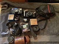 Overview photo of vintage cameras, lenses, accessories on gray towel including Vivitar 300Z Zoom, Leica AF, lenses, carrying cases