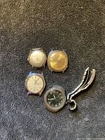 Four vintage watches with faces and cases on a black towel background