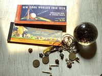 Photo of two World's Fair souvenir ticket books, one from 1939 New York World's Fair and one from 1949 San Francisco World's Fair, with various small collectible items arranged beside them including a glass paperweight.