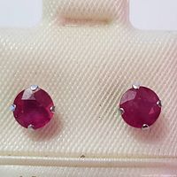 Close-up front view of the ruby earrings showing round faceted stones set in 10K white gold prongs.