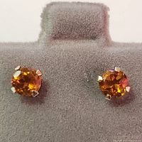 Close-up photo of 14K yellow gold stud earrings featuring round faceted citrine gemstones set in four-prong settings on a display stand.