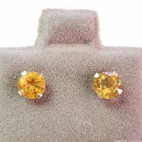 Pair of 14K yellow gold stud earrings with round faceted citrine gemstones on a gray display.