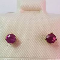 Close-up of front face of both ruby stud earrings showing the deep red color of the stones and the yellow gold prong setting.