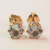 Front view of the pair of 9K yellow gold blue topaz stud earrings showing the round blue topaz gemstones in prong settings.