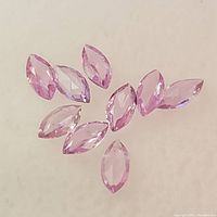 Nine marquise-shaped pink sapphire gemstones arranged on a white background, showing color and cut detail.