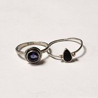 Two sterling silver rings; one with a round purple faceted stone, the other an open design with a black teardrop accent and silver beads