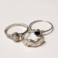 Three silver rings displayed closely together showing different stones and carved detail.