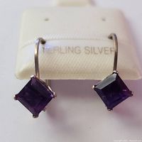 Front view of the sterling silver earrings with visible amethyst stones and hook wires on a display card marked 'STERLING SILVER'.