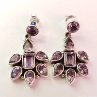 Front view of a pair of silver drop earrings with multiple amethyst stones in round, rectangular, and teardrop shapes arranged in a floral pattern.