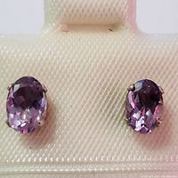 Front view of two oval amethyst stones set in sterling silver prong settings showing faceted stones and color.