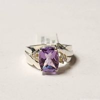 Front view of silver ring showcasing rectangular cushion-cut amethyst center stone with small clear accent stones on either side.