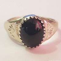 Front view of silver ring with oval black onyx stone and engraved decorations on band.