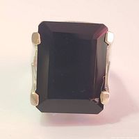 Close-up photo of the large rectangular black onyx set into the silver ring, showing the stone's faceted edges and four-prong setting.
