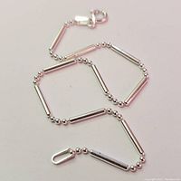 Silver bracelet laid flat showing cylindrical and round bead pattern, and spring ring clasp.