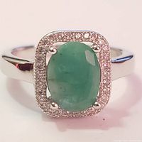 Front view showing oval green emerald colored stone with rectangular CZ halo in a silver band.