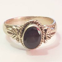 Front view of silver ring with faceted oval garnet stone and decorative leaf motifs.