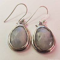 Close-up photo of front side of silver moonstone drop earrings showing faceted oval stones and silver bezels.
