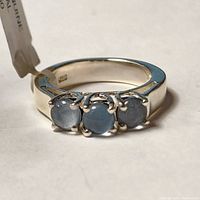 Close-up of the silver ring with three round blue-gray opal triplet stones set in prong settings, showing the polished silver band and stone details.