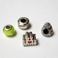 Four Pandora style beads arranged on white background clearly showing varied designs including glass, flower pattern, layered cake and piano shaped bead