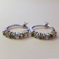 Front view of the silver hoop earrings showing alternating peridot (green) and white topaz (clear) round stones set on the front face.