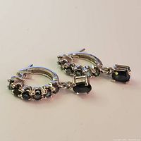 Pair of silver hoop earrings with small and larger dangling sapphire stones, shown on white background.