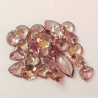 Cluster of approximately 24 faceted gemstones in light pink and purple hues, various shapes and sizes visible.