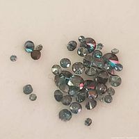 Close-up of loose treated blue diamonds scattered on a flat surface showing their small round faceted cuts and blue-gray color.