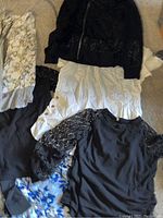 Full top-down view showing all blouses, some layered overlapping on a carpeted floor, showing different textures and colors including floral and lace details.