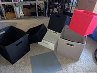 Six fabric foldable storage containers displayed on carpet, in black, gray, and red with handles