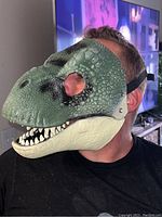 Side view of the green and beige textured T-Rex mask worn by a model showing the closed mouth and detailed surface.