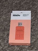Front view of the box showing the peach-colored 8BitDo USB Wireless Adapter 2 with brick pattern design and branding.