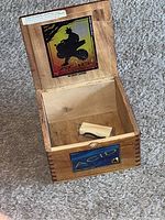 Photo showing wooden cigar box open with wooden roller inside, decals on lid and front showing silhouette and ACID brand