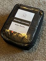 Original sealed packaged vest inside a black zippered carry case with clear top. User guide on top of packaging.