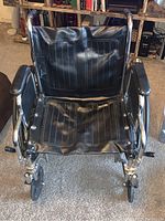 Front view of the black faux leather foldable wheelchair showing seat, armrests, footrests, and front wheels