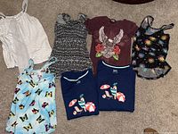Seven women's tops on floor: striped, patterned tanks; graphic tees; printed tanks.