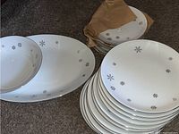 Stack of various sized white china plates and bowls with silver snowflake pattern and silver trim