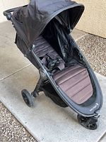 Front-side angled view of black Baby Jogger stroller showing padded seat, canopy, safety harness, and front wheel.