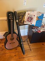 Full view of guitar standing in open hard case next to music stand with sheet music displayed