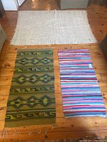 Top-down photo showing all three rugs laid out on wooden floor: the large cream rug, the green Southwestern patterned rug, and the colorful striped rug.